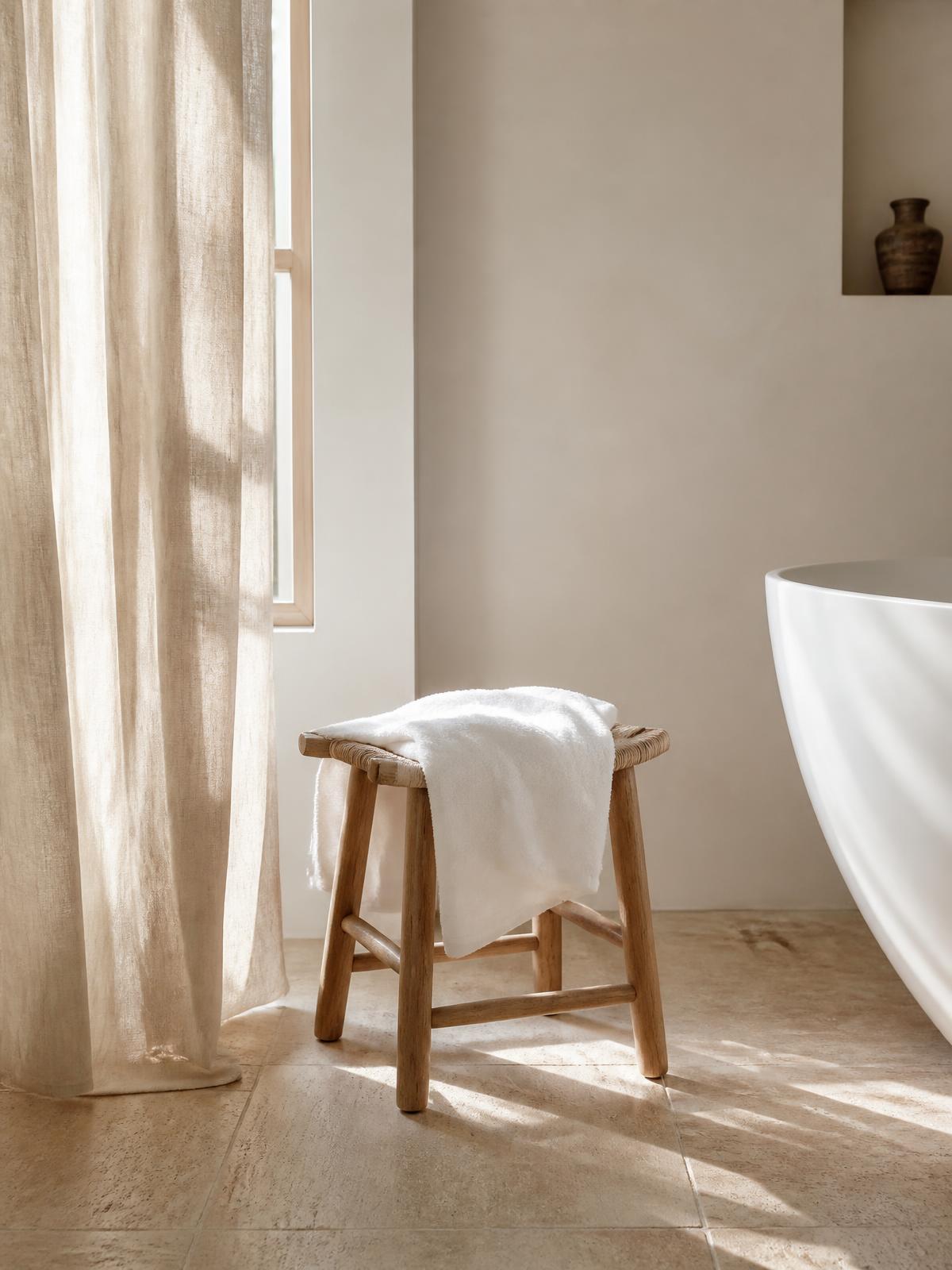 Sunlit minimal bathroom with a white towel on an oak stool